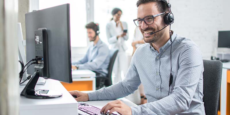 Ein lachender, junger Mann mit Headset sitzt am Computer